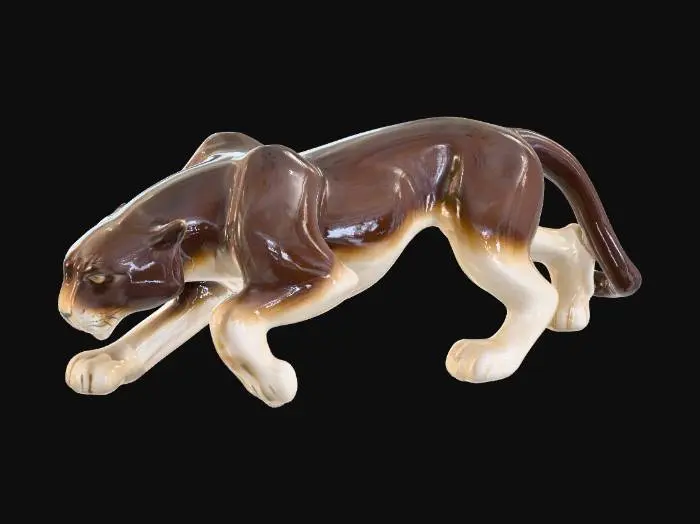 3D model for A lithe ceramic panther figurine, captured in a dynamic, low-crouching pose, poised to pounce. Its slim, powerful body is adorned with a glossy two-tone glaze; a deep, polished espresso brown covers most of its form, while a soft, creamy beige highlights its underbelly, inner legs, and muzzle. The sculpture features smooth, cool curves with no visible texture, showcasing sleekness and predatory elegance.