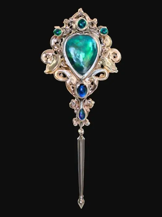 3D model for A Victorian-style hair pin, primarily crafted from polished sterling silver, features a central oval-shaped mother of pearl inlay with a subtly iridescent sheen. The silver frame is intricately sculpted with delicate filigree scrollwork, accented by tiny, bezel-set emeralds at each cardinal point and small, deep blue sapphires nestled within the curves of the design, giving it a luxurious, antique appeal.