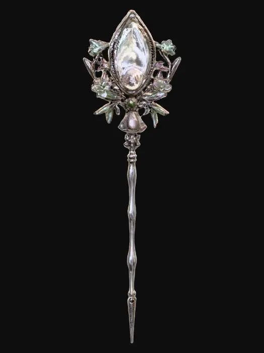3D model for A long, slender hair pin, characteristic of Victorian elegance, features a silver body intricately embossed with floral motifs. The head of the pin is adorned with a large, teardrop-shaped mother of pearl piece, exhibiting a creamy white color with faint pink and green overtones. It is framed by a delicate border of minute, square-cut emeralds and tiny, round sapphires, creating a captivating sparkle.