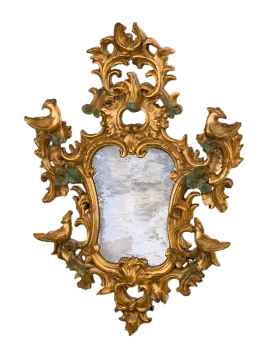 3D model for An ornate, antique gilded mirror featuring a rococo style frame. The frame is crafted from aged, slightly distressed wood, textured with intricate carvings of scrolling acanthus leaves and flourishes, exhibiting a rich, dull gold finish with hints of darker patina in the crevices. Four distinct, finely detailed bird figures with textured feathers are perched symmetrically on the upper and lower sides of the irregularly shaped, reflective glass pane, adding to its elaborate, sculptural appearance.
